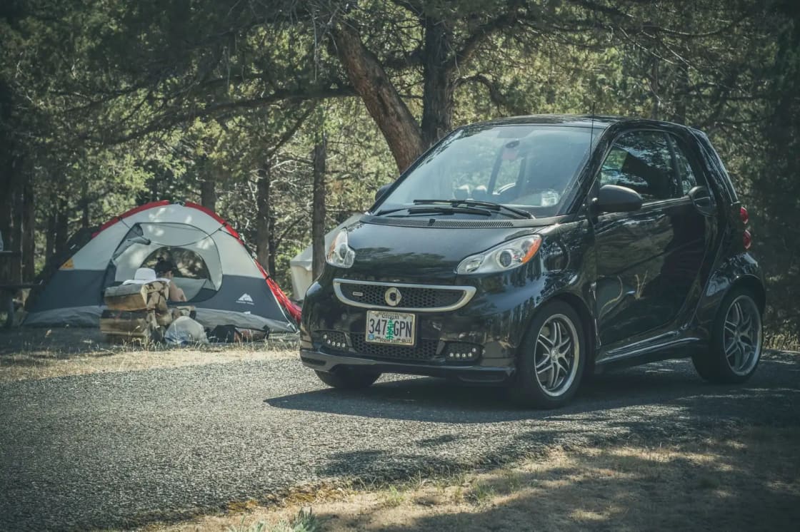 Smart car parked beside a tent in a wooded campsite, perfect for outdoor adventures