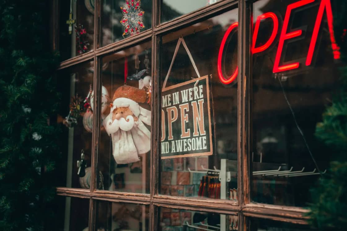 A shop window decorated for the holidays with a Santa ornament, a hand-lettered open sign and a red neon glow