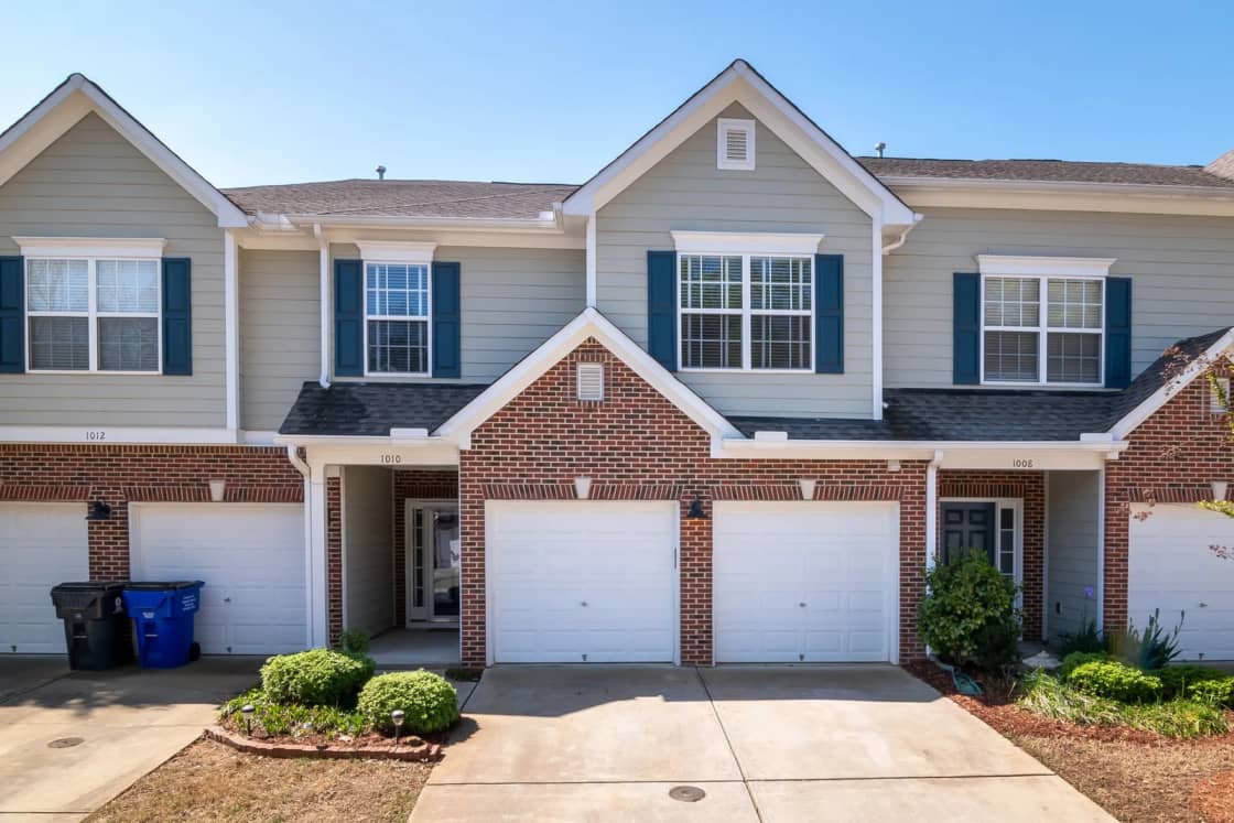 A row of two-story townhomes with white garage doors, gray siding and small front yards.
