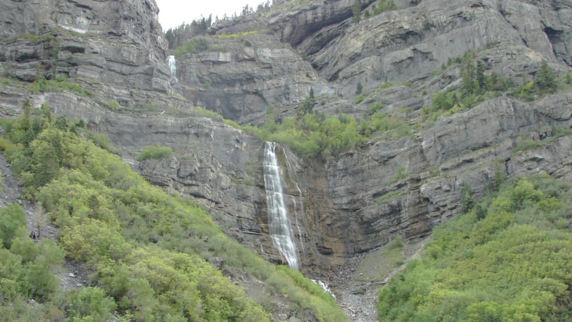 Bridal Veil Falls pouring down a gray limestone cliff in Provo Canyon between slopes of green scrub