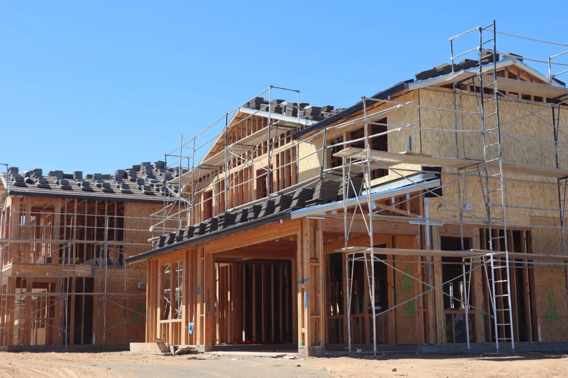 A new house framed in wood and wrapped in scaffolding as construction continues under a clear sky.