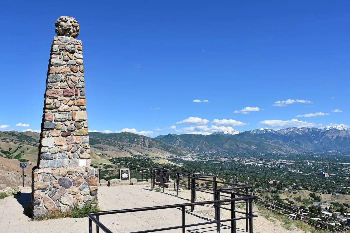 The stone monument on Ensign Peak beside a railed viewing area, with downtown Salt Lake City and the Wasatch Range spread out below