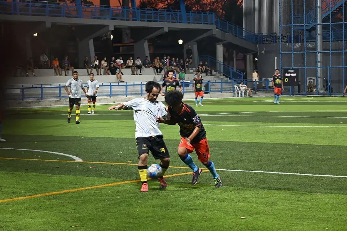 Two soccer players battling for possession during an evening match on a grass field