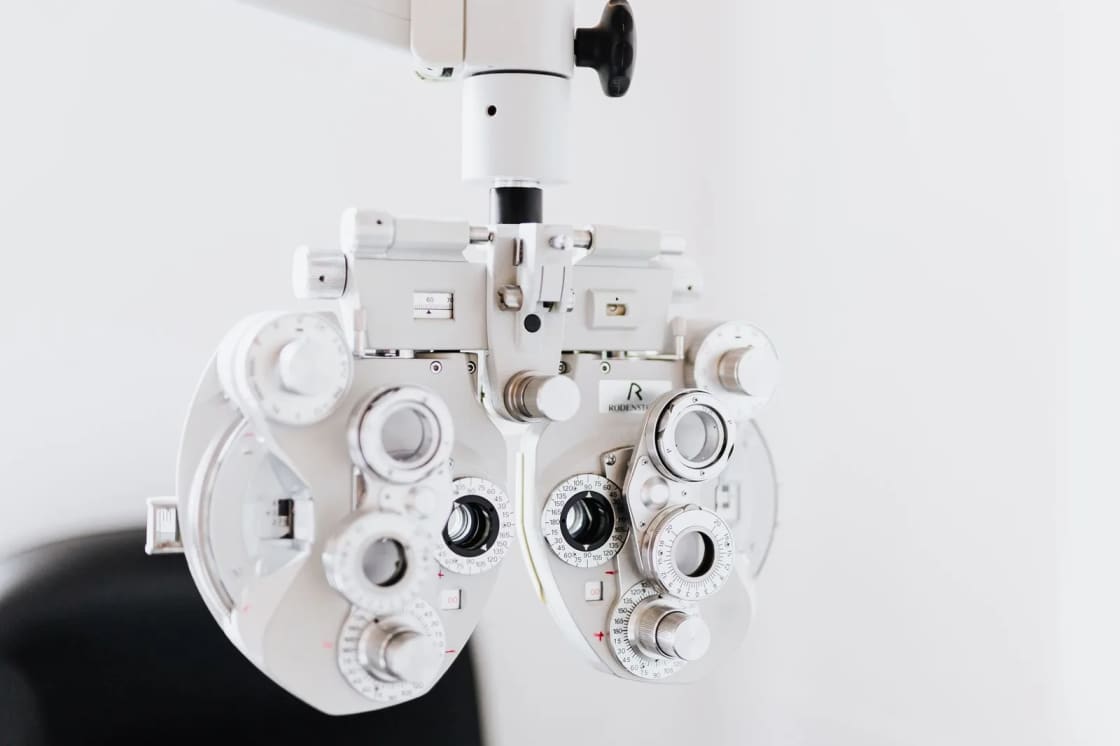A white phoropter, the multi-lens instrument used to measure a glasses prescription, against a pale background