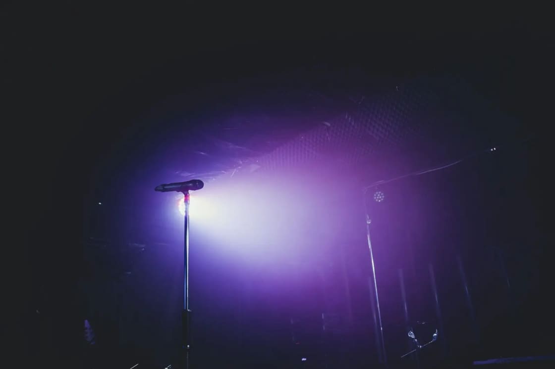 A moody stage setup with a microphone under purple lighting, perfect for concerts