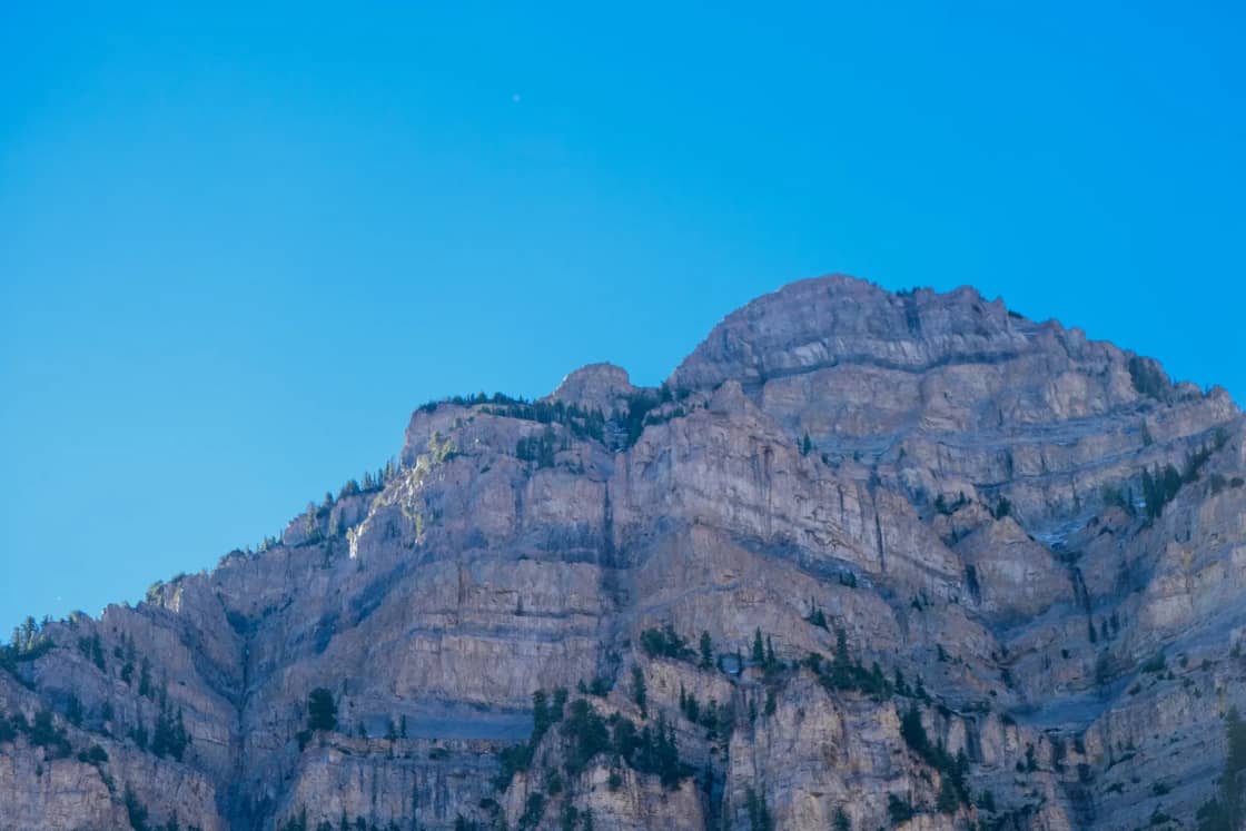 A sheer gray limestone mountain face lit by low winter sun against a clear, pale blue December sky.