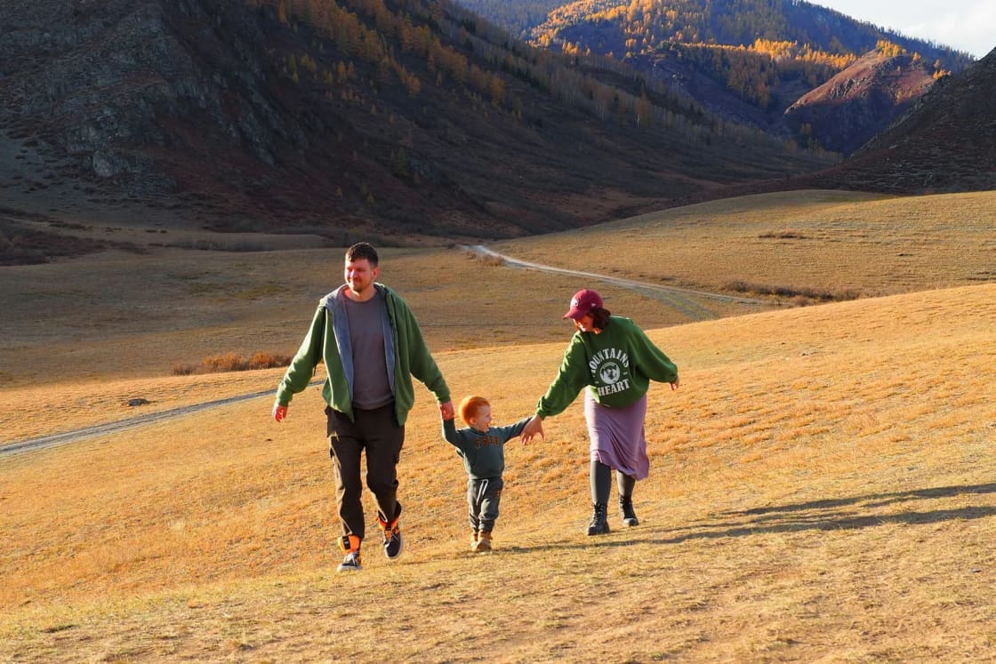 A mother, father and small child walking hand in hand up a dry grassy slope in a wide mountain valley