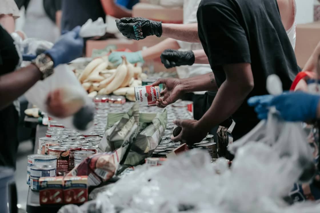 Volunteers in gloves sorting canned goods and bagged produce along a long table at a food drive