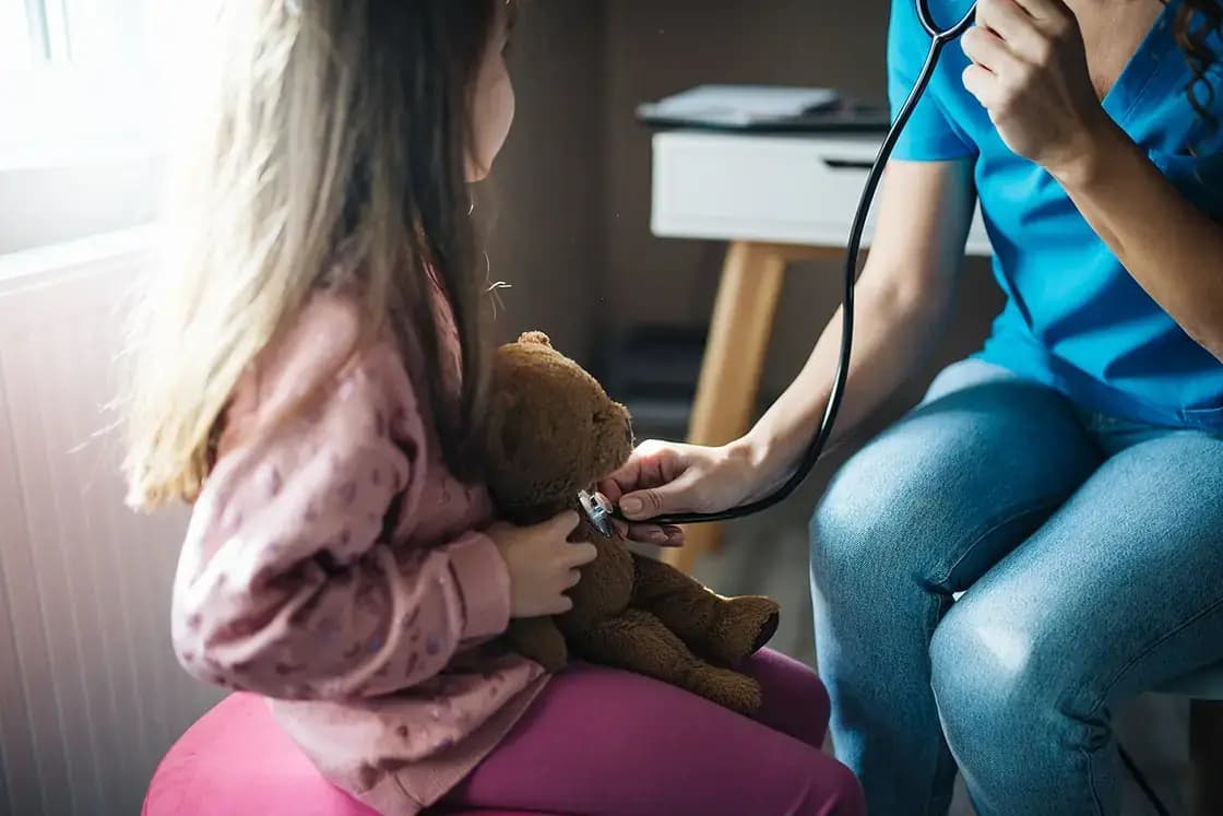 A doctor holds a stethoscope to a teddy bear during a child's checkup