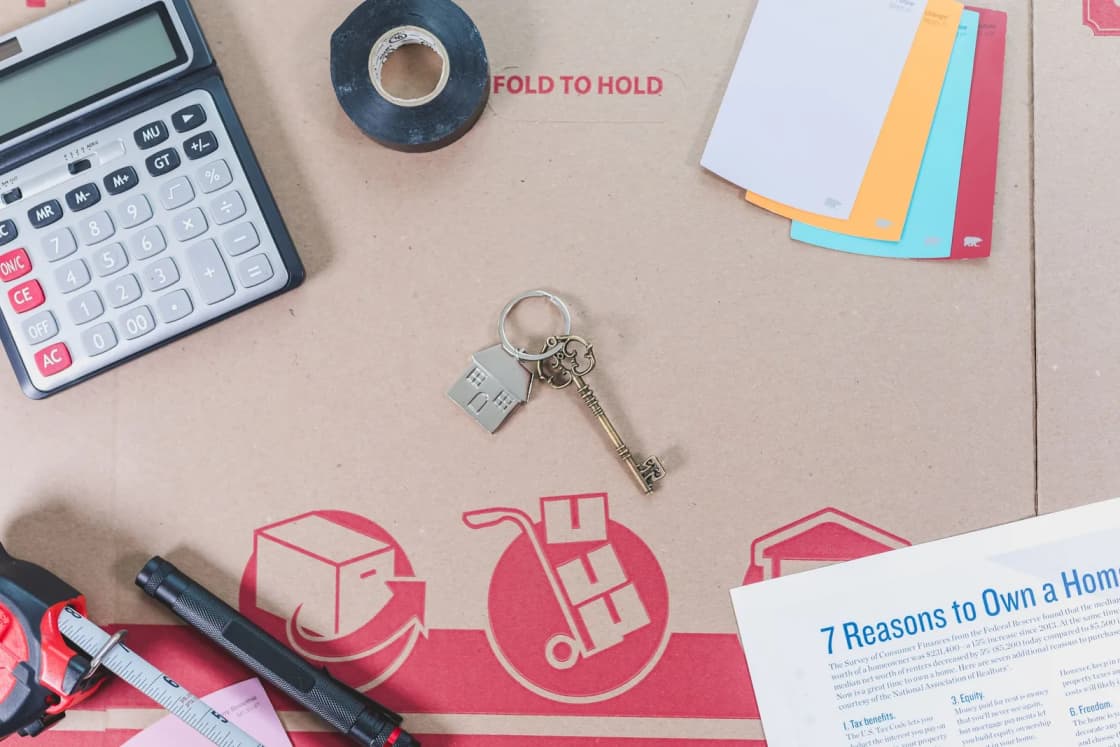 House keys, a calculator and a homebuying pamphlet laid out on a desk.
