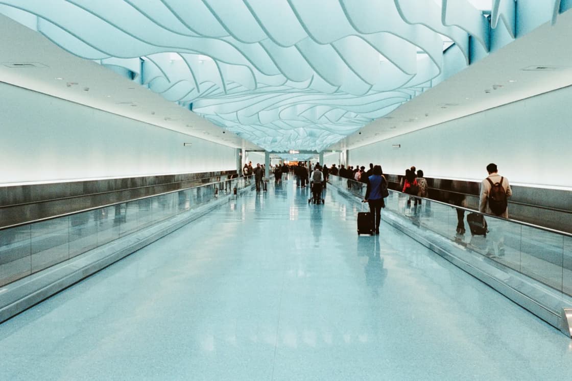 Travelers with suitcases ride the moving walkways down a long Salt Lake City International Airport corridor under a wavy, blue-lit ceiling.