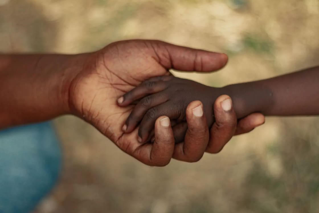 An adult hand and a child's hand clasped together outdoors against a blurred background
