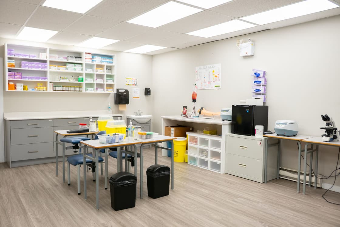 A bright clinic supply room with stocked wall shelving, a central work table and stools