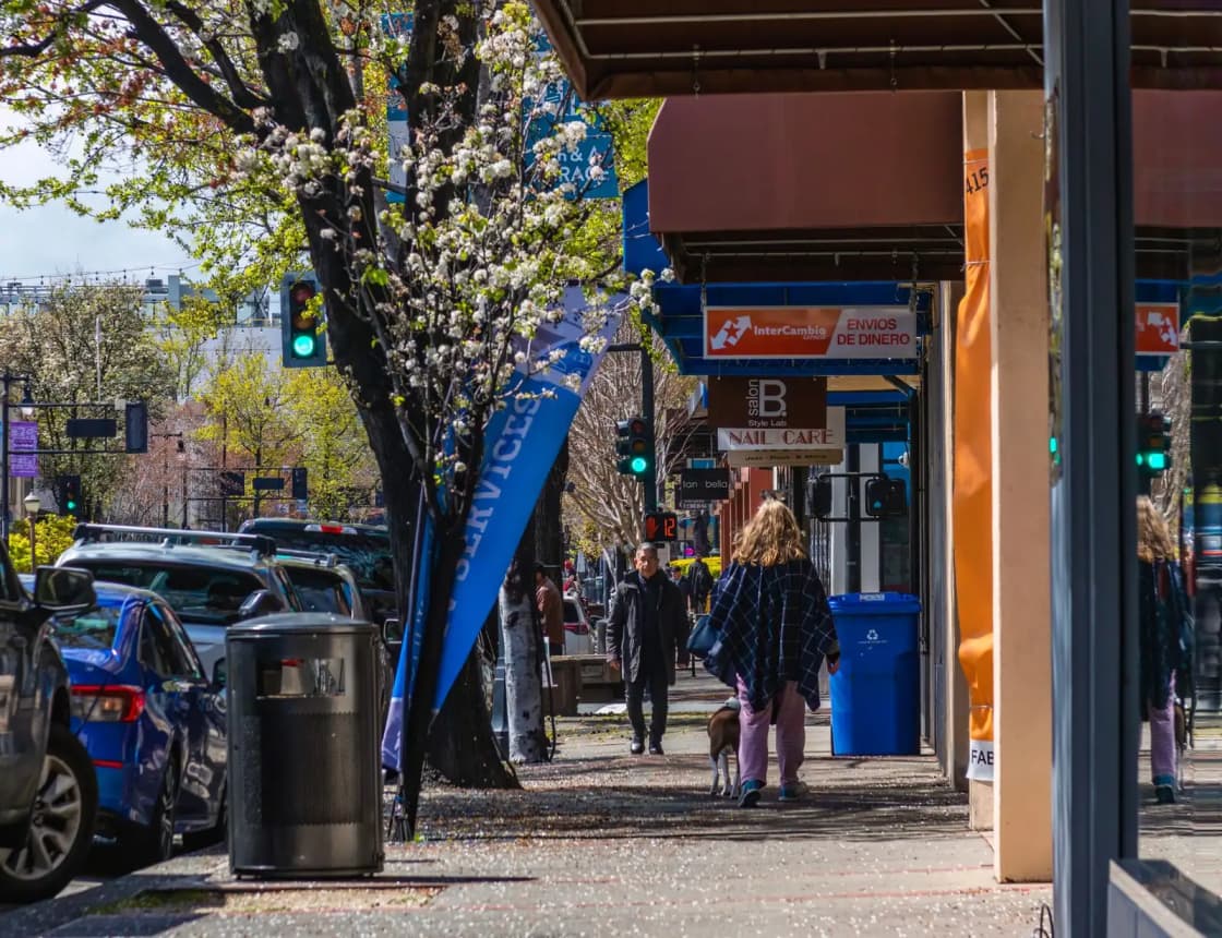 Vibrant urban scene showing people walking on a busy street lined with cars and storefronts