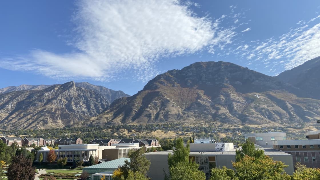 Brigham Young University's campus in Provo beneath the peaks of the Wasatch Range under a sky of feathery white clouds