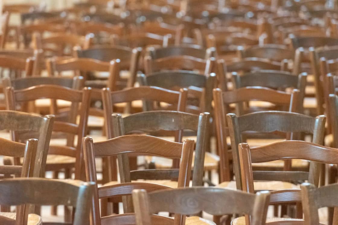 Rows of empty wooden rush-seated chairs set out in a hall