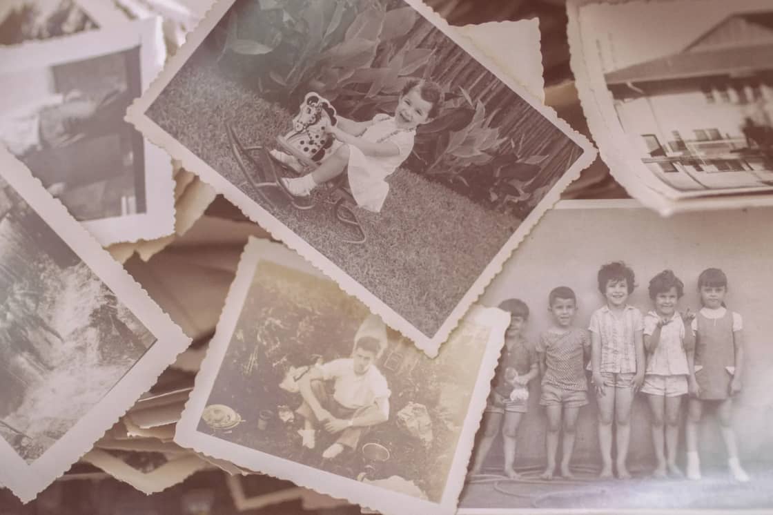 A loose pile of vintage black-and-white family photographs spread across a surface, including a group portrait of children