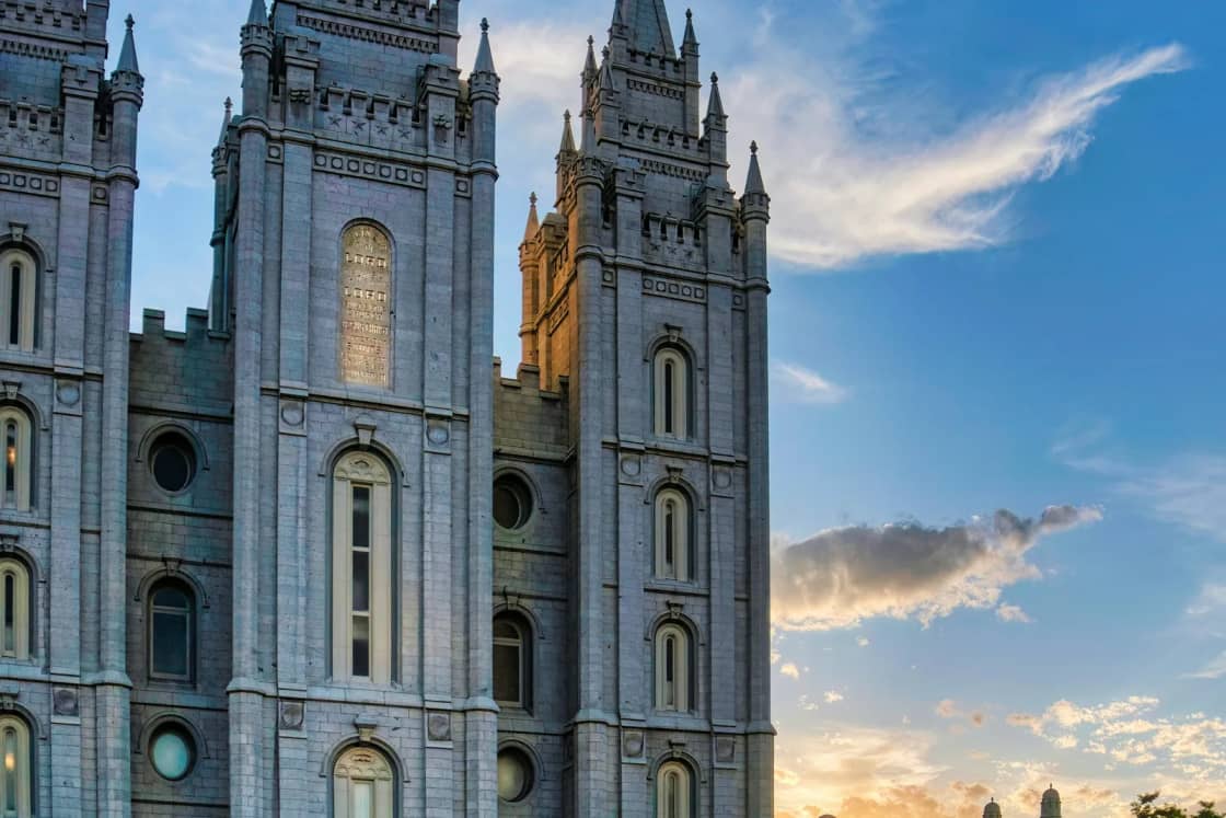 The granite spires of the Salt Lake Temple on Temple Square glowing at sunset, with a reflecting pool in the foreground.