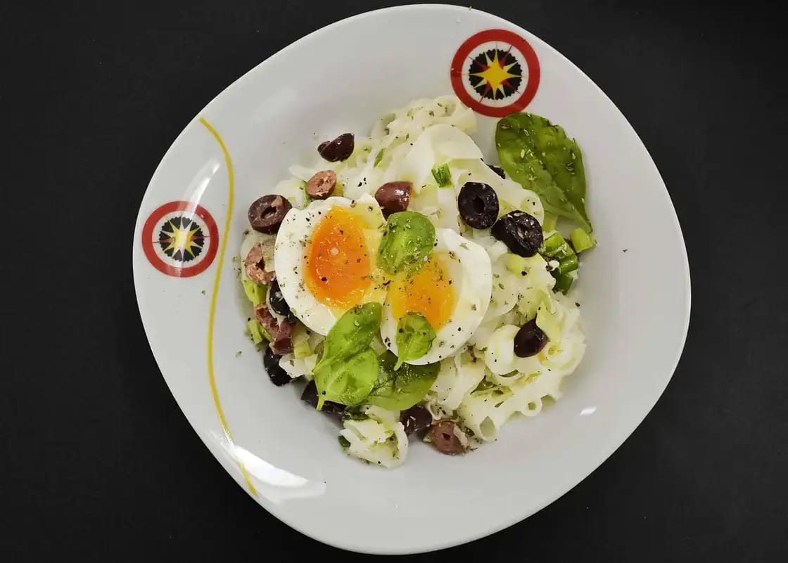 A plate of poached eggs with avocado, olives and greens