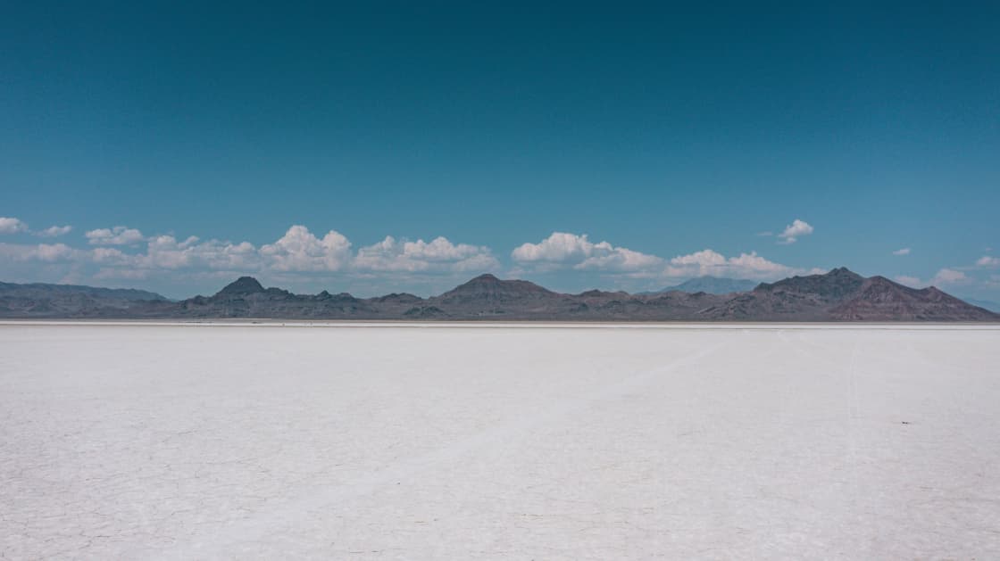 A vast flat expanse of white salt crust stretching to distant mountains under a wide sky
