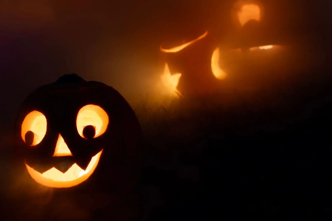 Carved jack-o-lanterns glowing orange in a dark, foggy yard at night, one grinning face in front and more lit shapes behind it