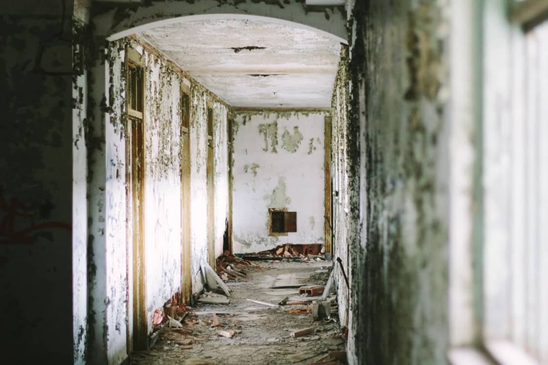 An abandoned corridor with peeling paint, exposed doorways and rubble scattered across the floor