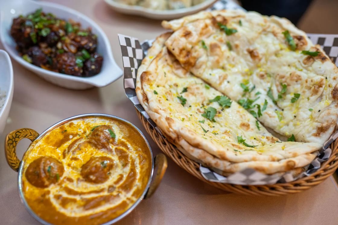 Curry dishes and naan bread served in baskets on a table