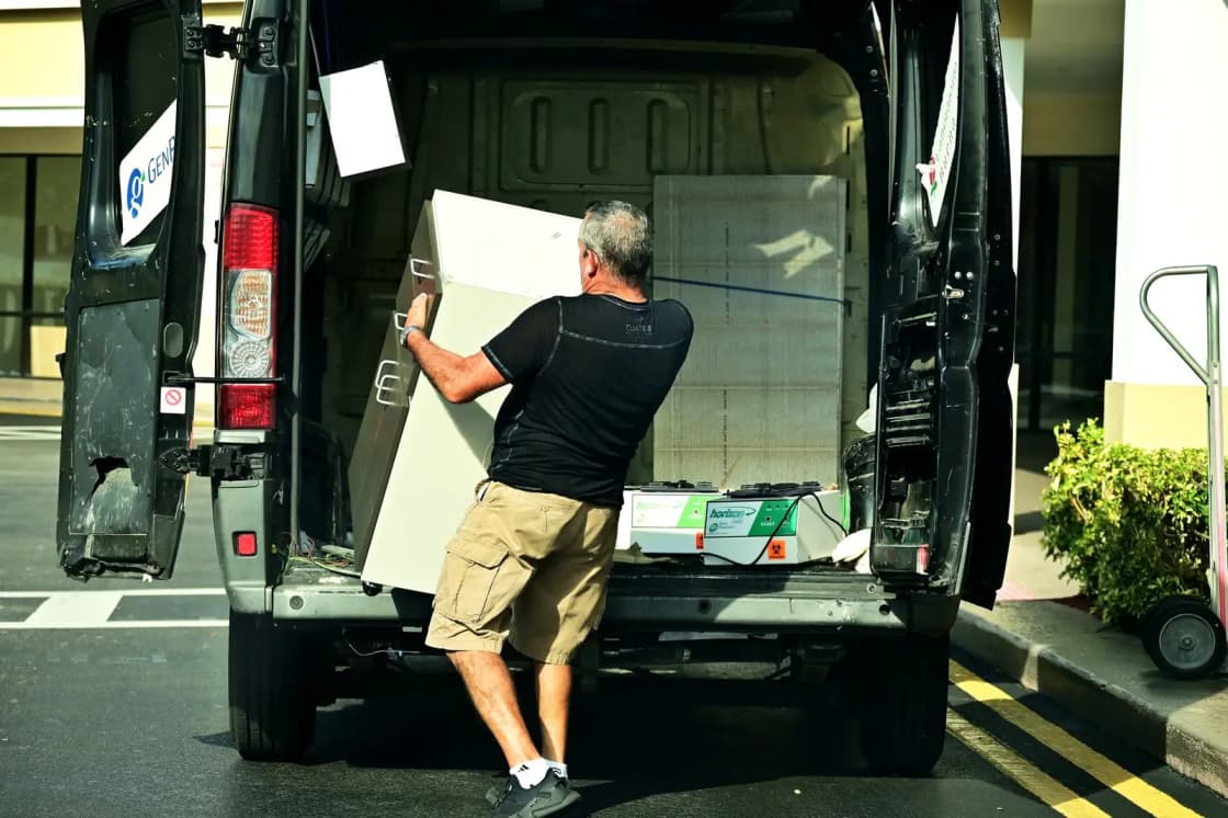 Two movers in uniform carrying stacked cardboard boxes through a bright, empty room