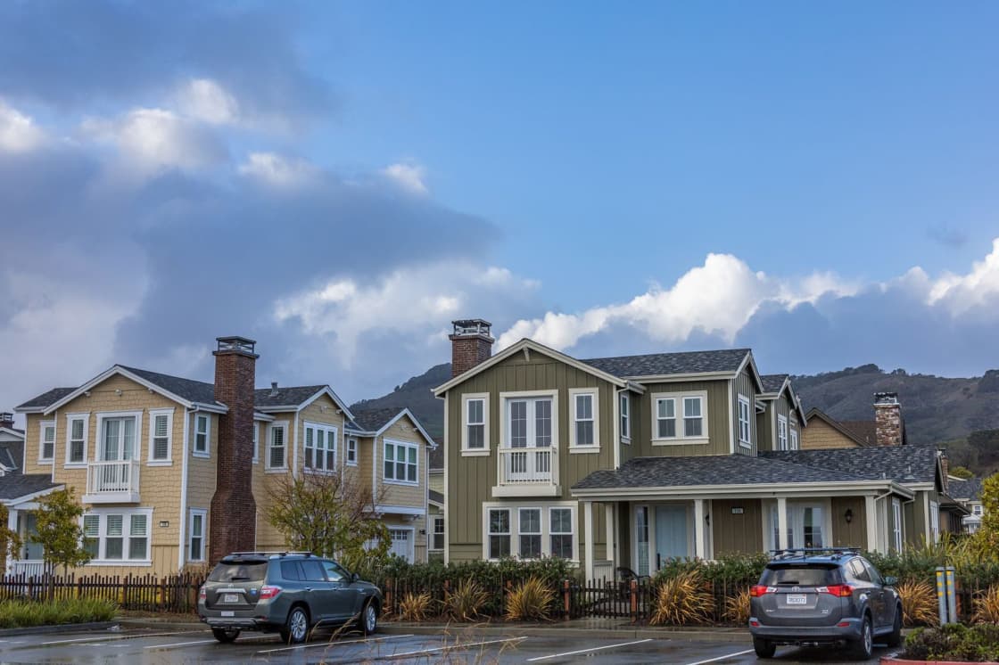 Two-story houses with front porches and brick chimneys along a street, with hills rising behind them