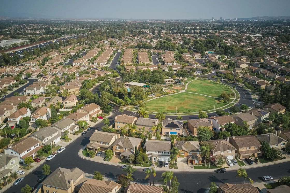 An aerial view of a planned neighborhood of houses curving around a central park and ball field.