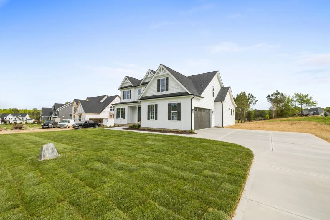 A white two-story farmhouse-style home with a curving driveway and a freshly sodded lawn.