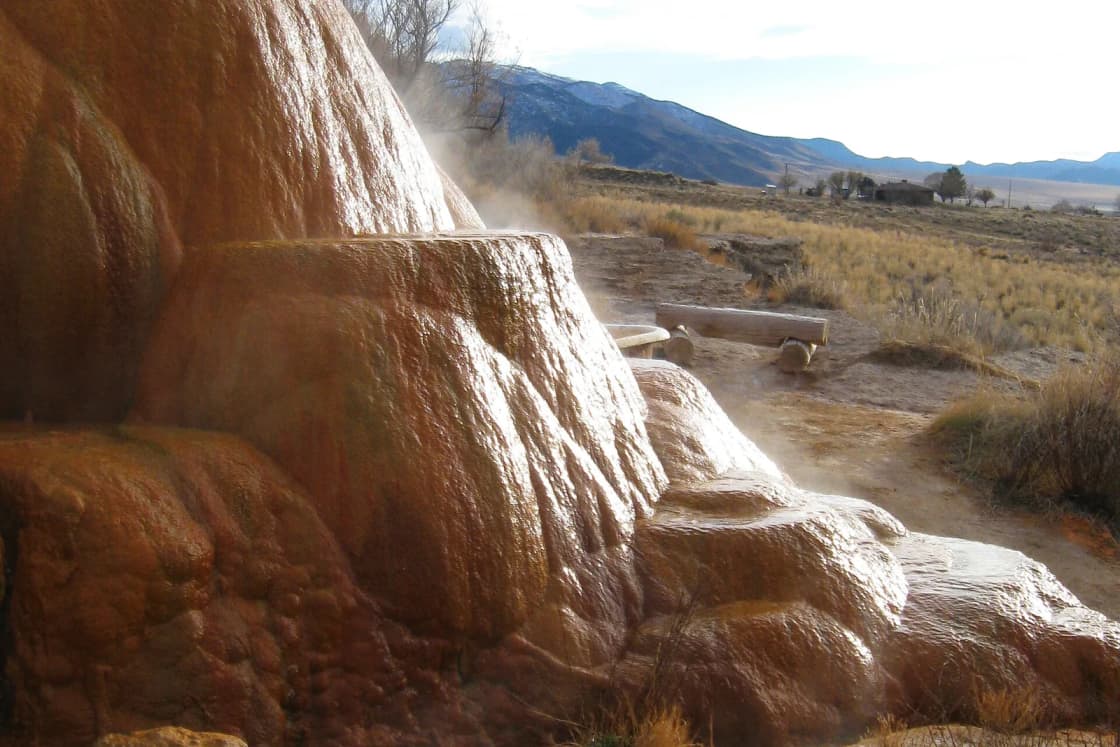 Steam rising off orange mineral terraces at Mystic Hot Springs in Monroe, Utah, with mountains in the distance.