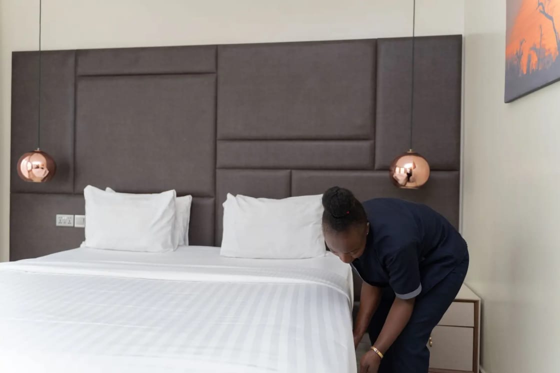 A hotel staff member prepares a bed in a sleek, modern hotel room with copper accents
