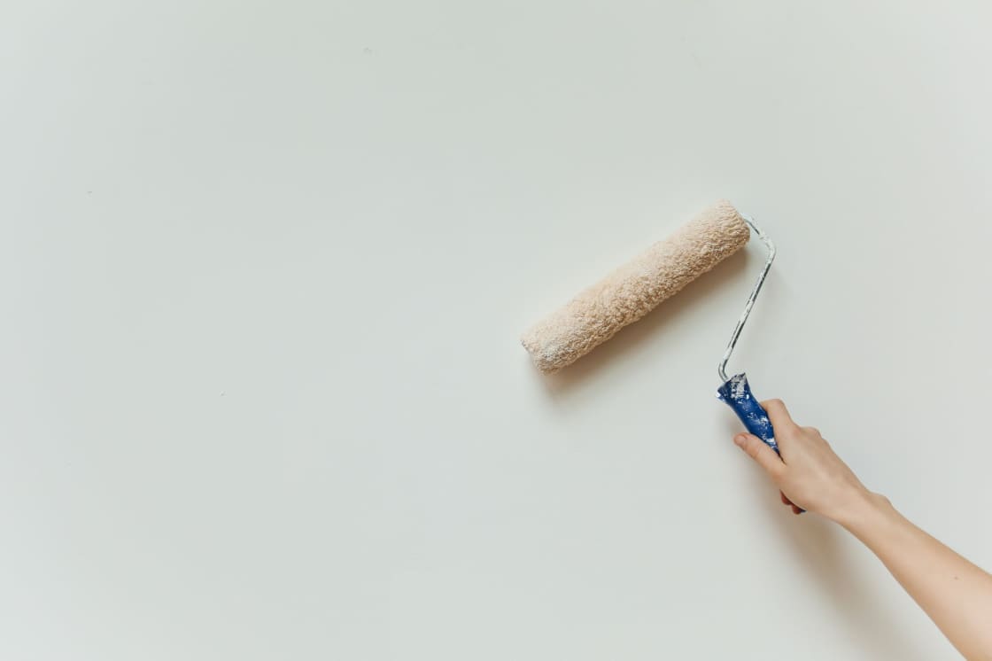 A hand holding a paint roller against a plain off-white wall