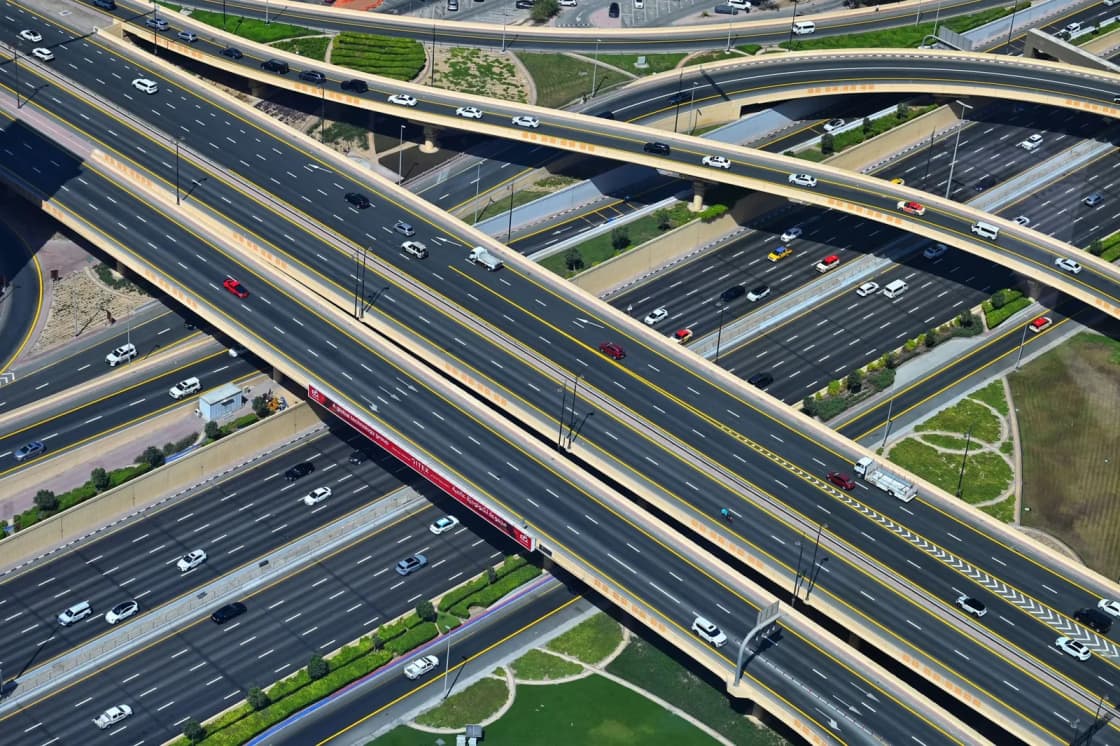 An aerial view of a multi-level freeway interchange, with sweeping ramps crossing above a wide multi-lane carriageway carrying traffic