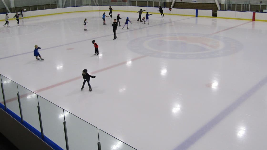 Children and adults skating a public session on the rink inside Peaks Ice Arena in Provo, seen from above the glass along the boards