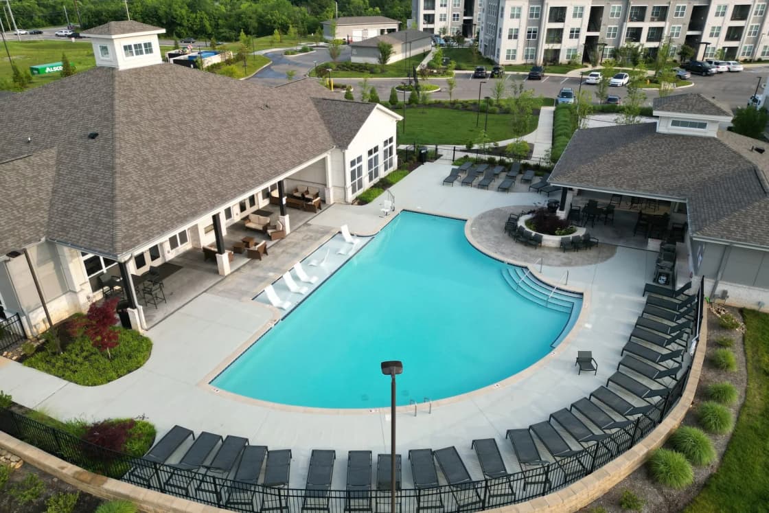 An apartment community's swimming pool with lounge chairs beside the clubhouse and apartment buildings.