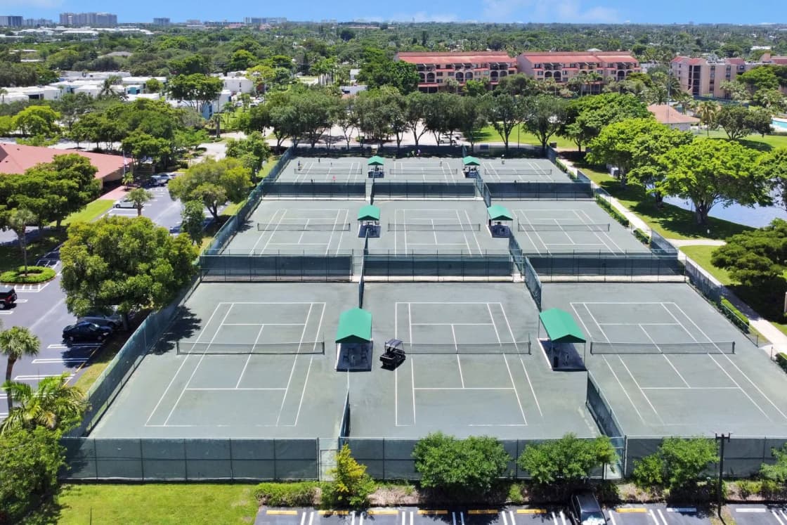An aerial view of a row of outdoor tennis courts surrounded by trees and buildings.