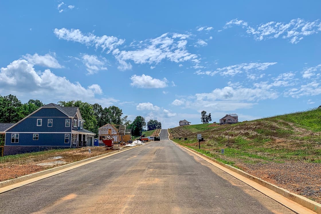 A newly paved subdivision street with fresh curb and gutter running uphill past houses under construction and graded lots