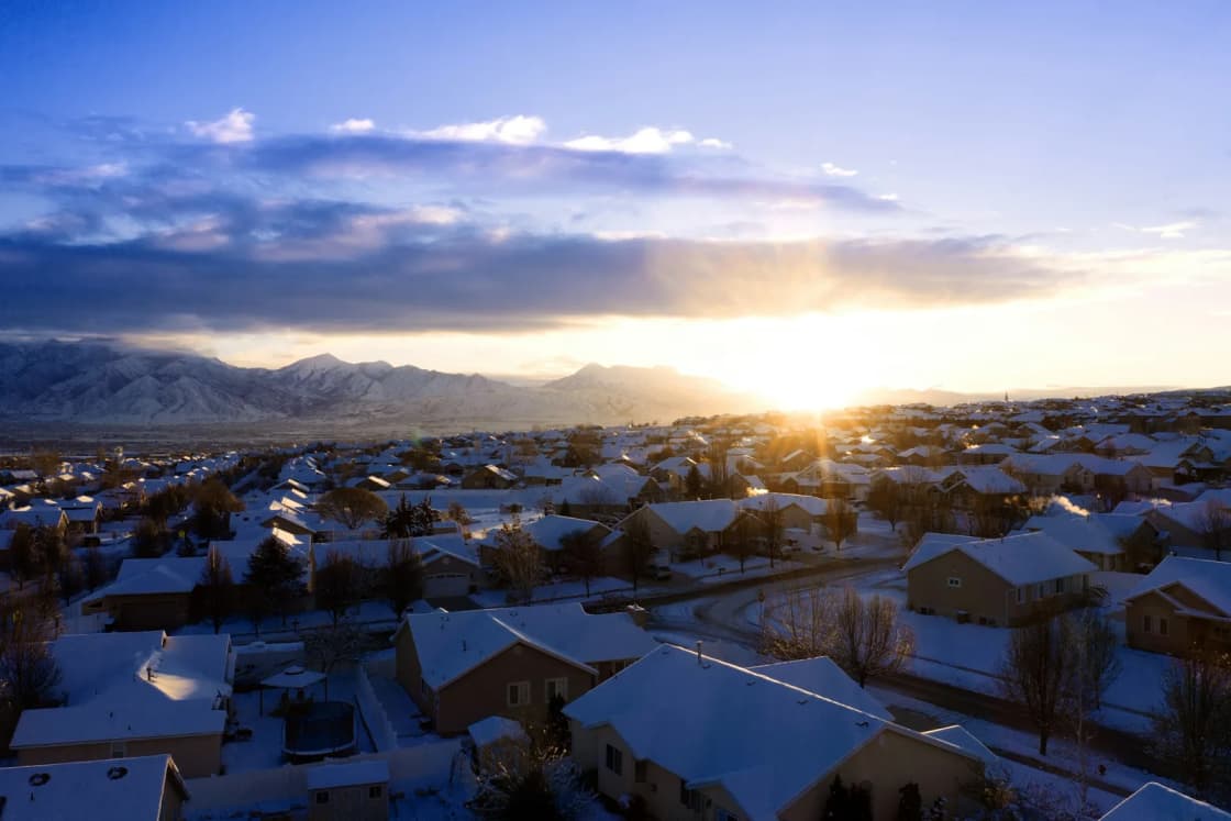 Snow-covered rooftops of a newer Herriman subdivision, next door to Daybreak, glow at sunrise with the Wasatch Range on the horizon.
