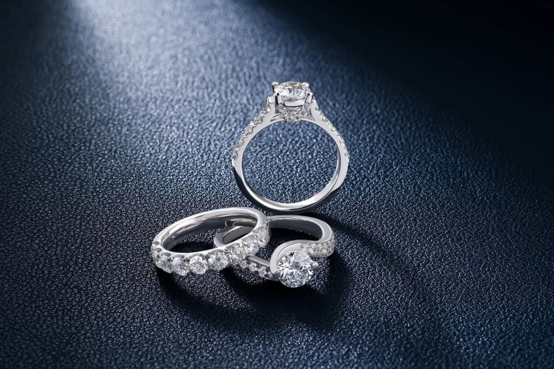 A diamond engagement ring and a matching band lying on a dark blue surface.
