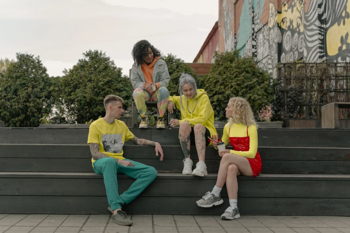 Four young adults in bright clothes sit and talk on wide concrete steps outside a building