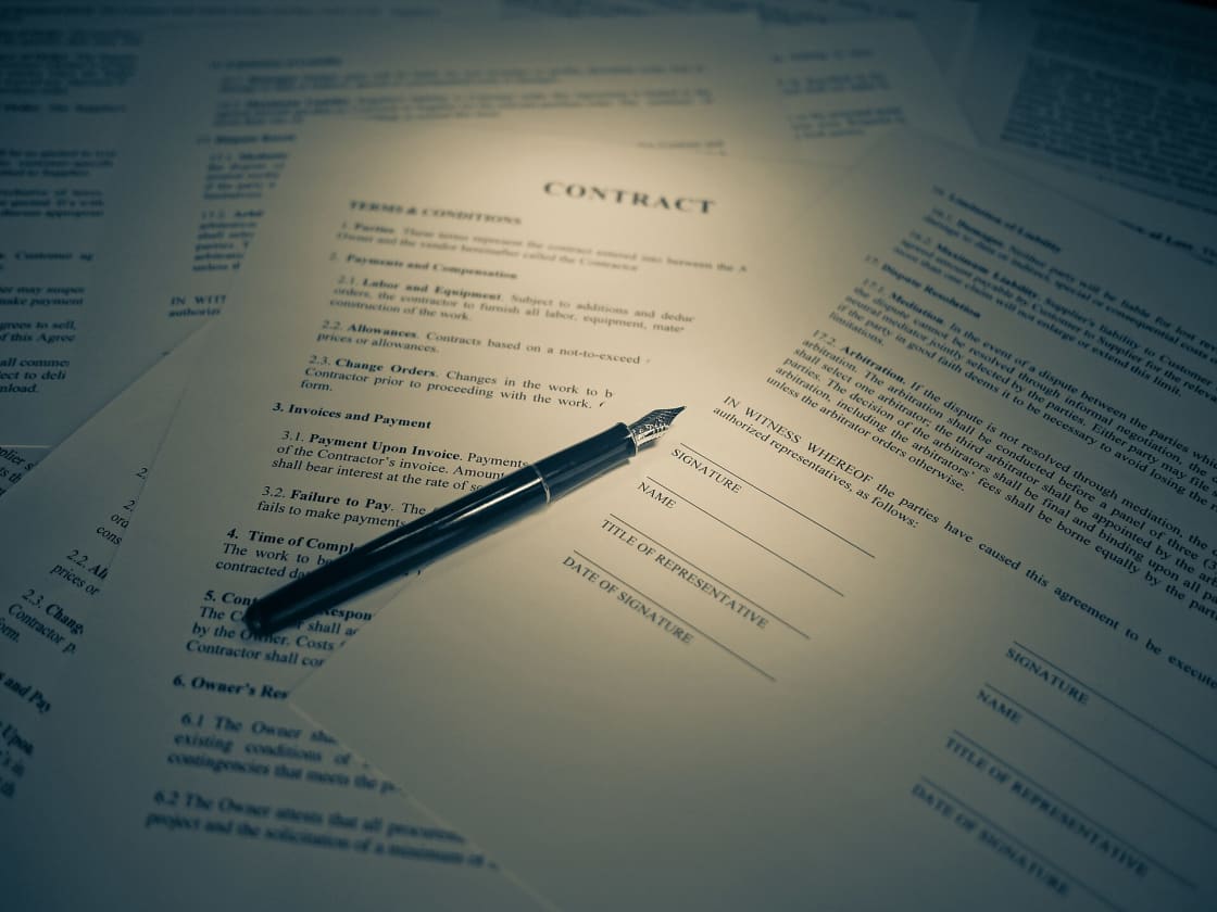 A dark fountain pen resting on a printed contract document with signature lines visible beneath it