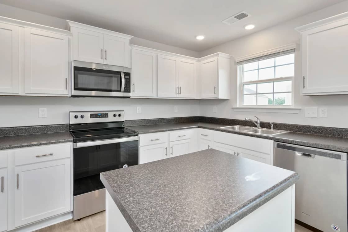 A new white kitchen with a gray stone island, stainless appliances and a window over the sink.