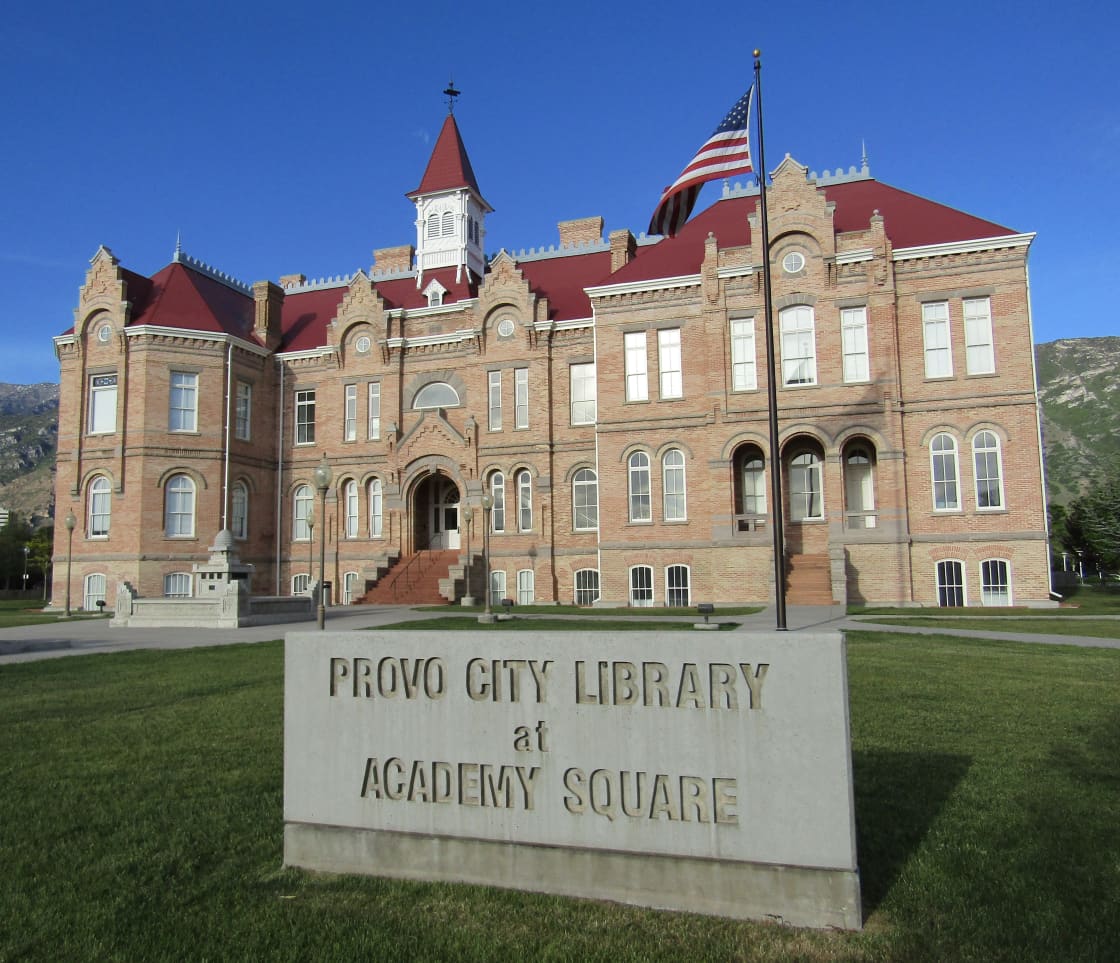 Red-roofed brick academy building behind a stone sign reading Provo City Library at Academy Square