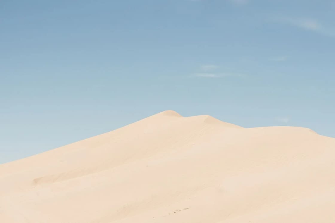 A smooth pale sand dune rising against a soft blue sky at Little Sahara Recreation Area near Nephi