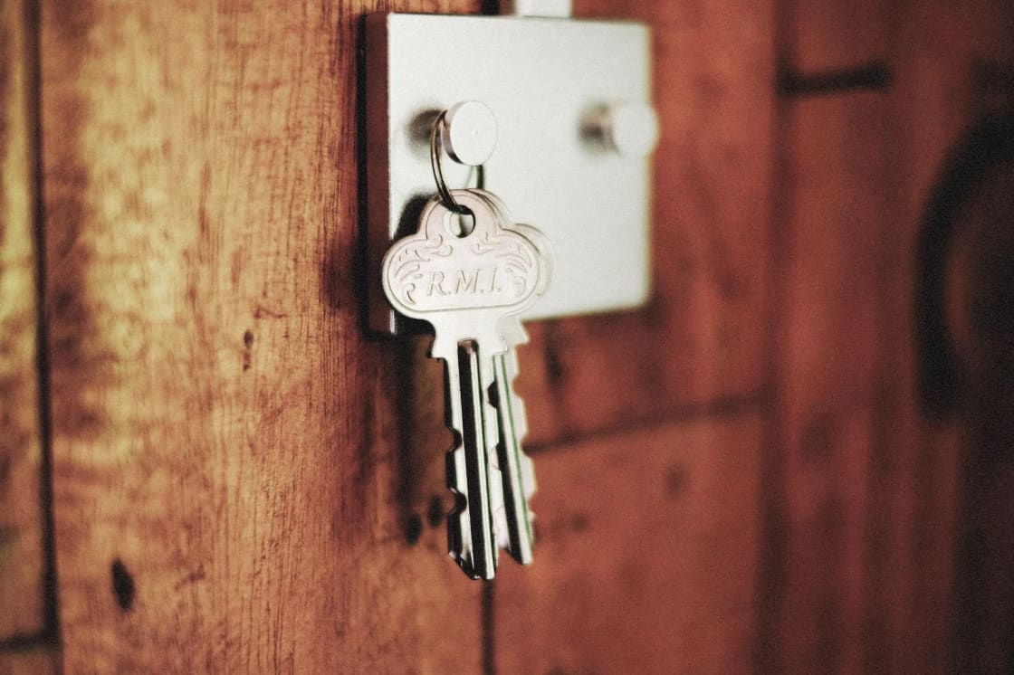 Keys hanging from the lock of a wooden door, with a decorative metal key fob