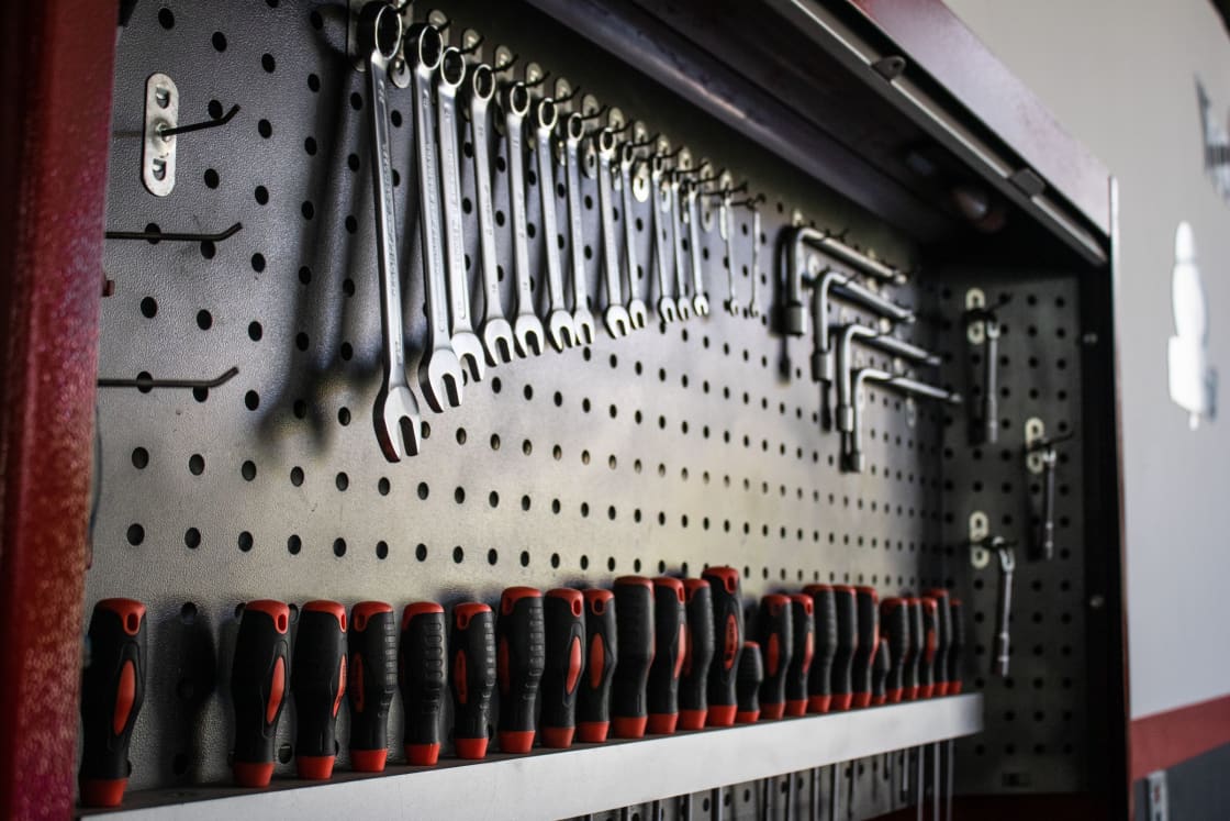 A workshop pegboard hung with a graduated row of combination wrenches and hex keys above a rack of red-and-black screwdriver handles