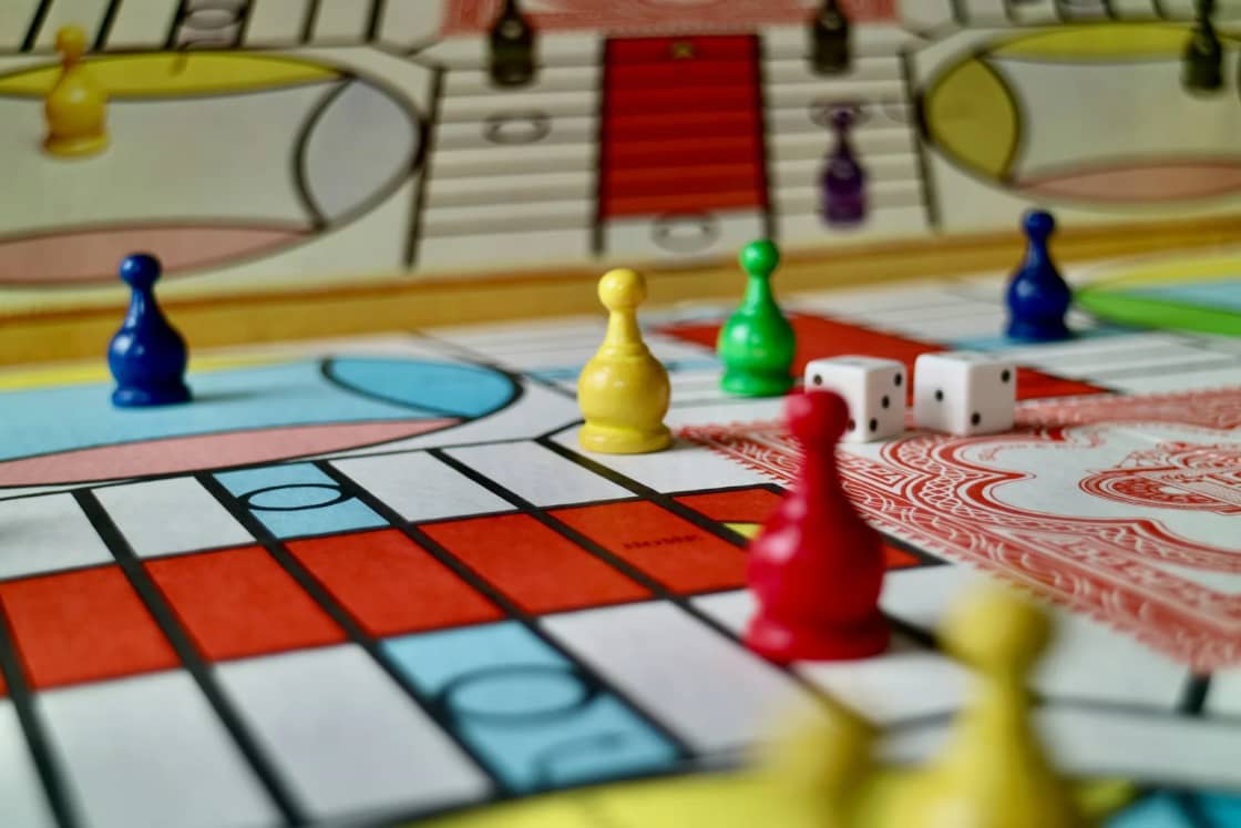 Colorful pawns and two white dice mid-game on a bright board game spread across a table