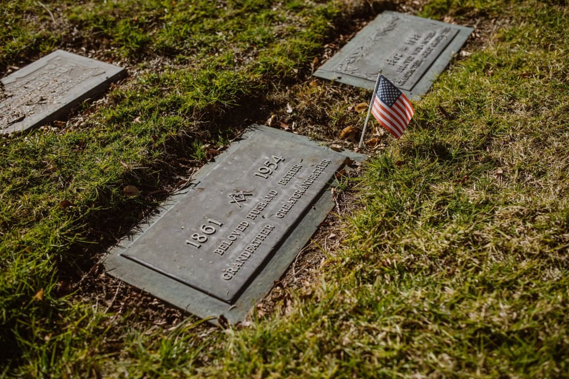 Two flat grave markers set in green grass with a small American flag beside them